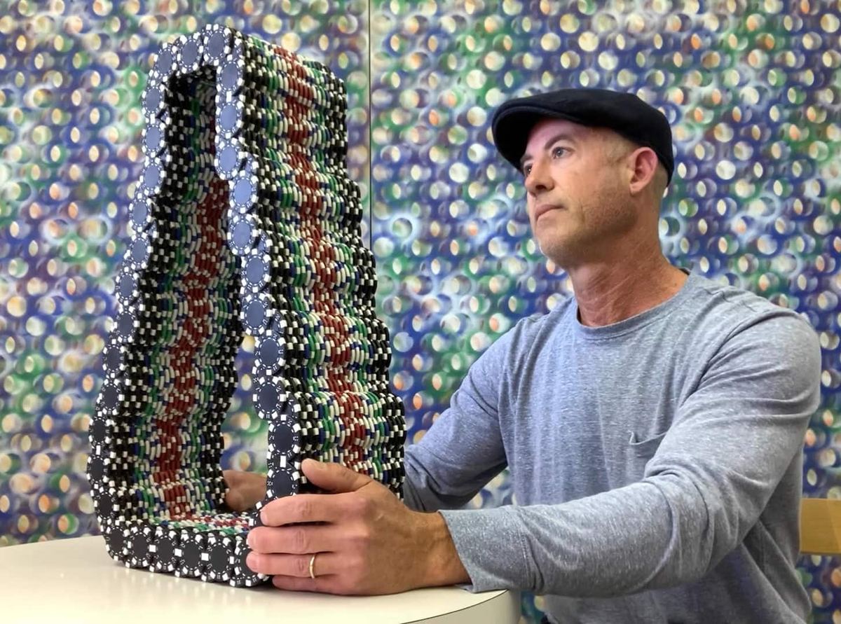 Stephen Giannetti in his Davis, California studio, holding one of his poker chip sculptures with one of his paintings on the wall behind him